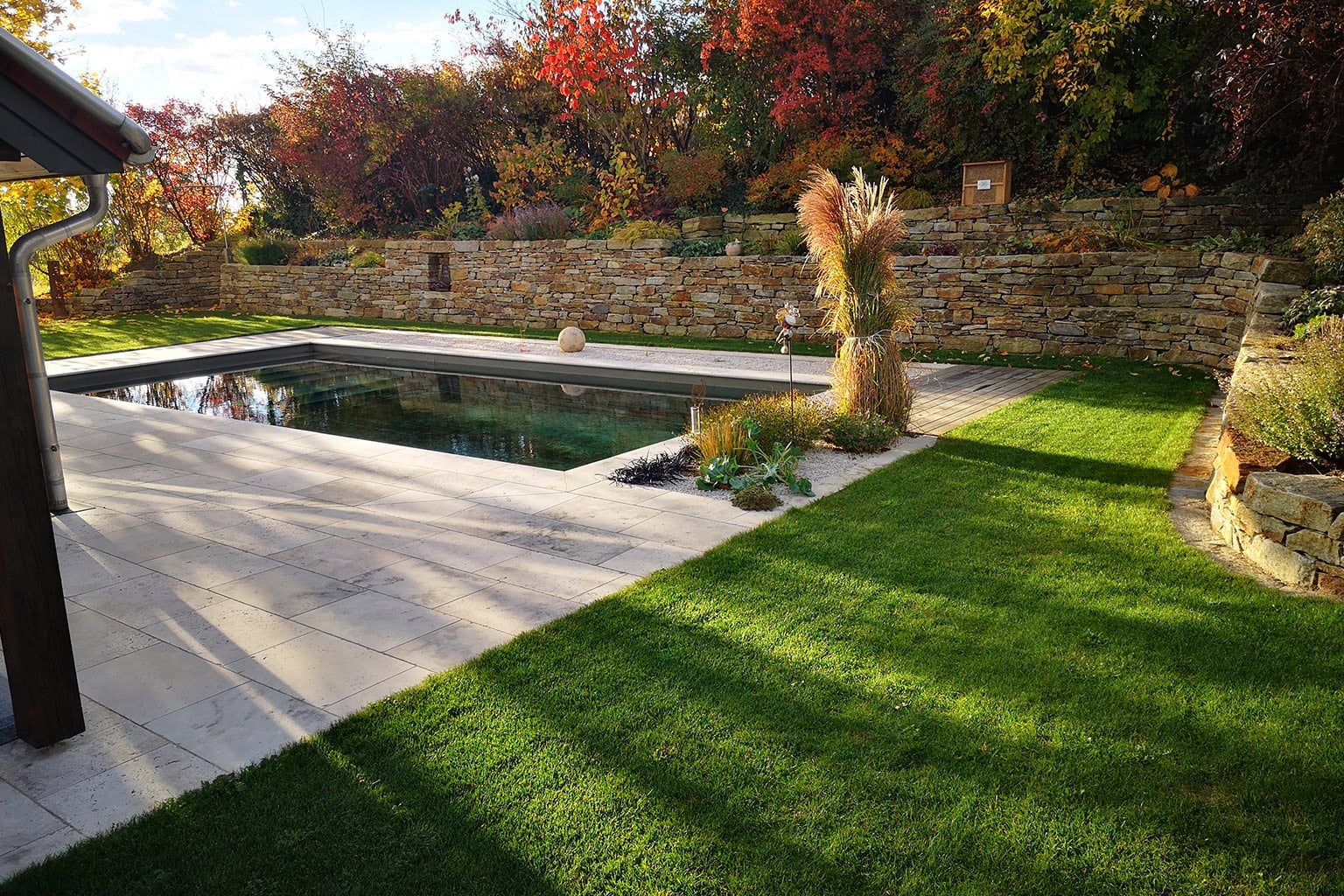 Moderner Garten mit Pool, Steinmauer, Terrasse und gepflegtem Rasen im Herbstlicht