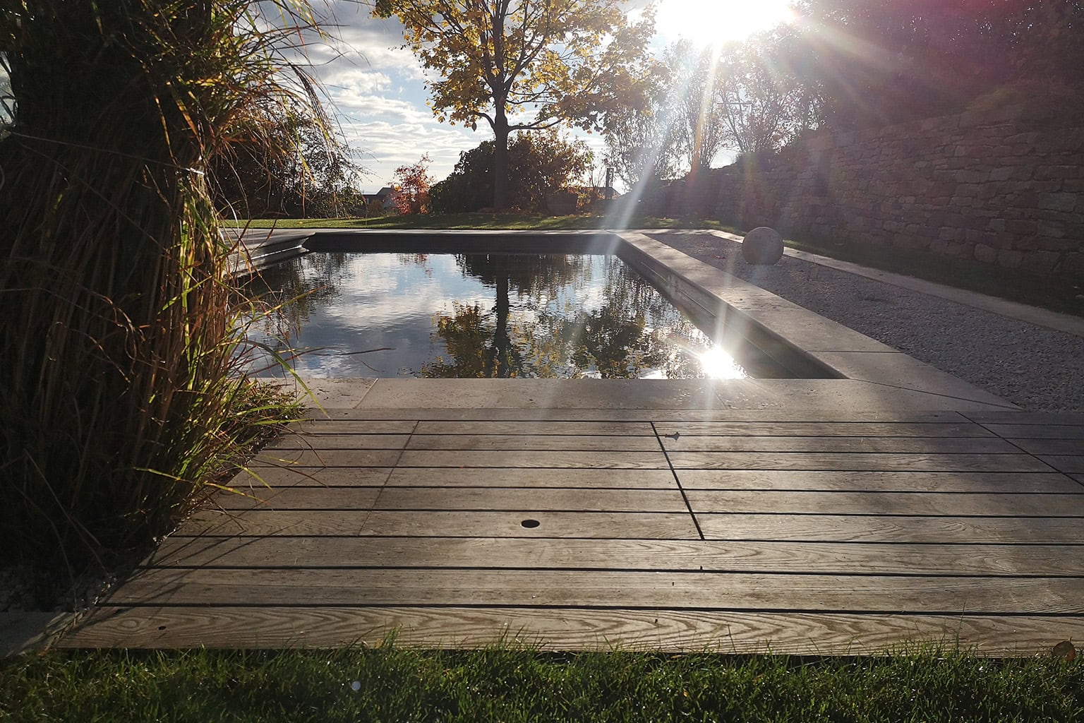 Moderne Poolanlage mit Holzdeck, Steinmauer und Sonnenschein im Garten