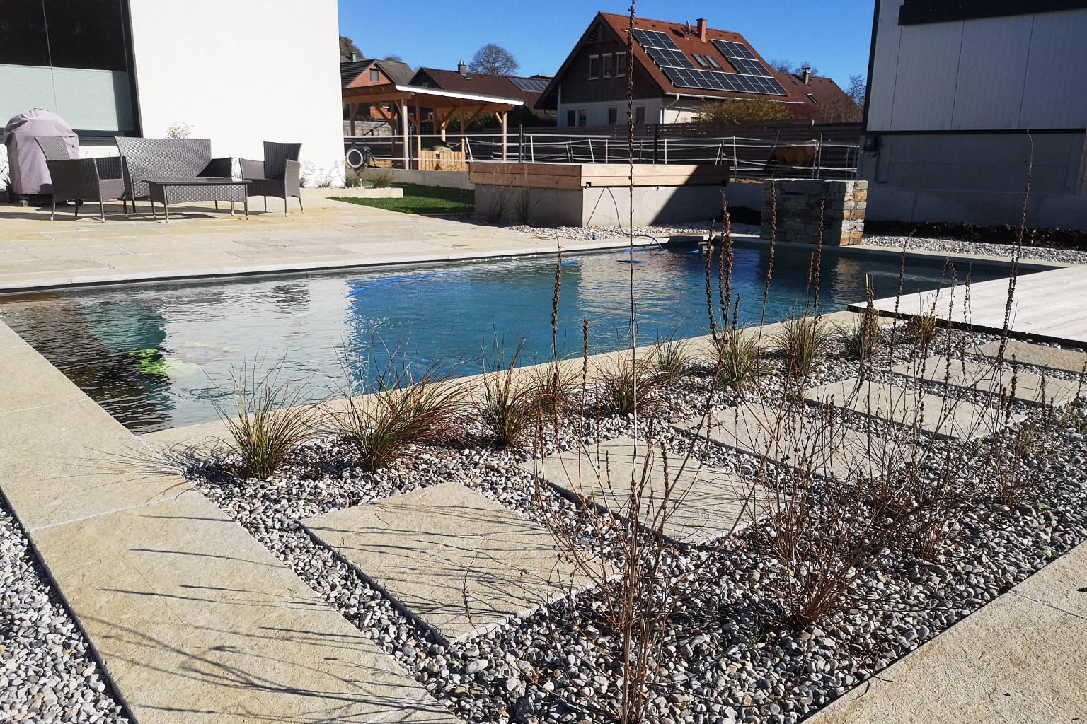 Modern gestalteter Garten mit Pool, Stegplatten und Sitzbereich vor einem Haus